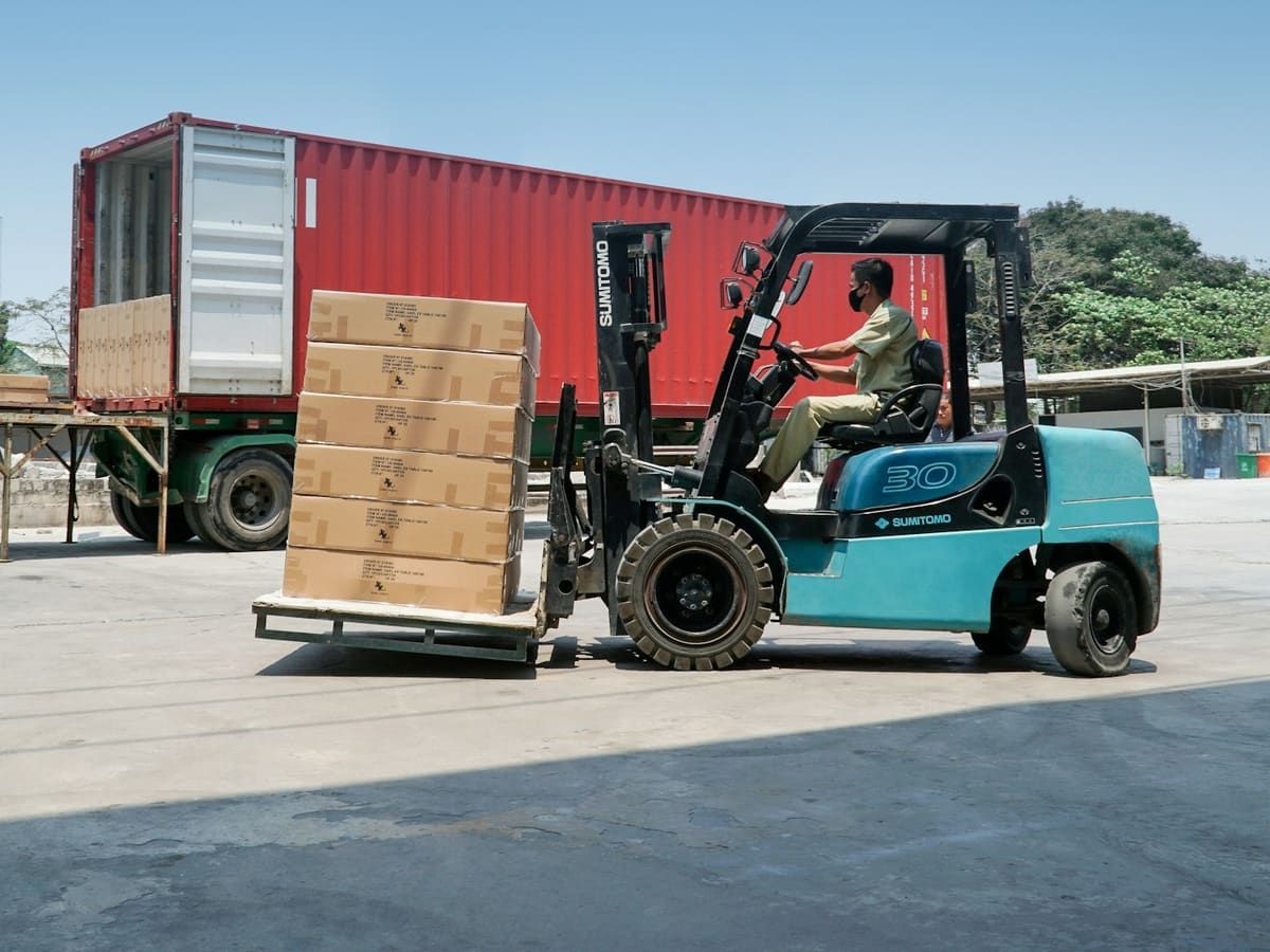 Forklift carrying a pallet of cartons to a container truck